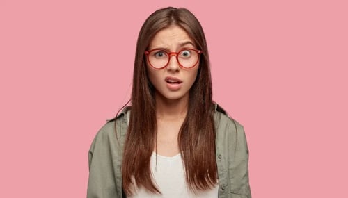 A woman wearing glasses stands against a vibrant pink background, showcasing her confident expression