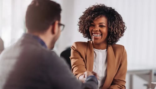 A woman and a man shaking hands in a modern office setting, symbolizing a professional agreement or collaboration