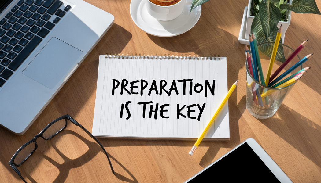 Office table with laptop and “preparation is the key” written on paper