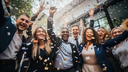 A diverse group of business professionals joyfully celebrating with confetti in a bright office setting.