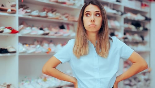 Female retail worker standing in front of shelves of shoes looking frustrated