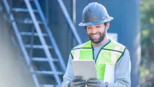 Male wearing hard hat and safety vest holding tablet