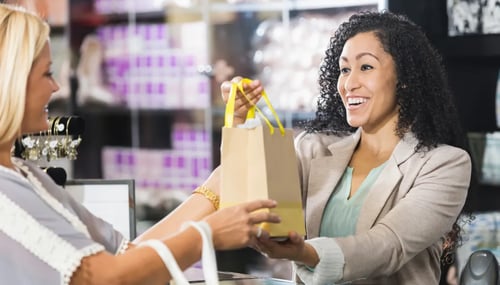 Female retail worker handing shopping bag to female customer